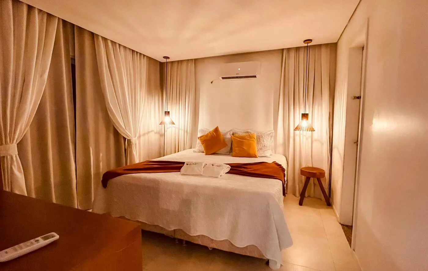 Suíte King Size com pendentes de madeira e cortinas claras