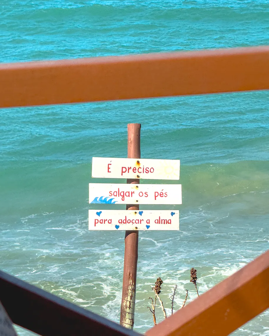 Placa de madeira indicando o caminho para o mar entre vegetação